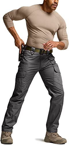 Man wearing dark gray tactical cargo pants with an olive green belt, multiple side pockets, and a smooth ripstop-style fabric. Paired with a tan long-sleeve shirt and light brown boots.