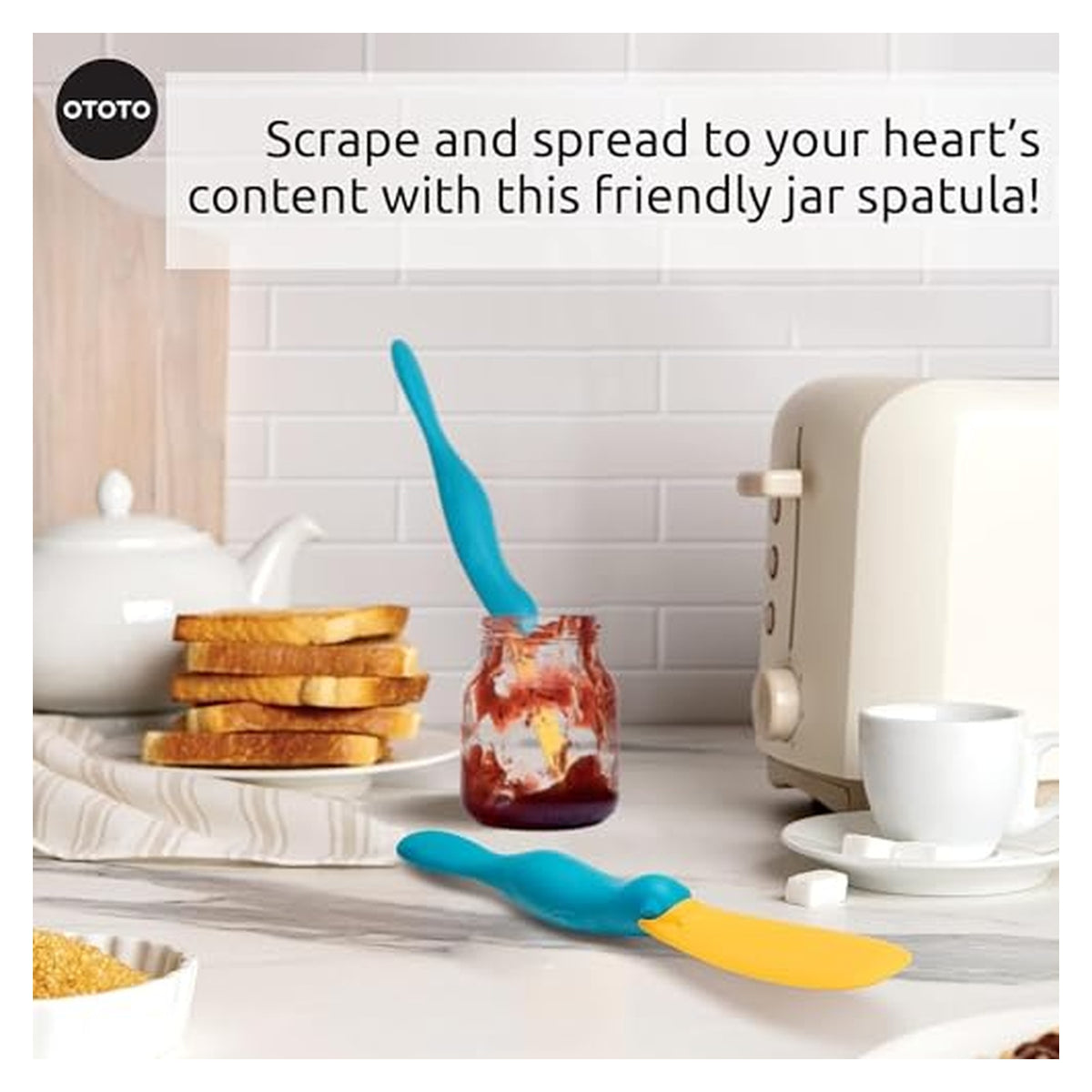 OTOTO jar spatula in teal and yellow, shaped like a platypus, shown in a kitchen scene. One spatula scrapes inside a jam jar, another lies flat on the counter. Text reads: 'Scrape and spread to your heart's content with this friendly jar spatula!'