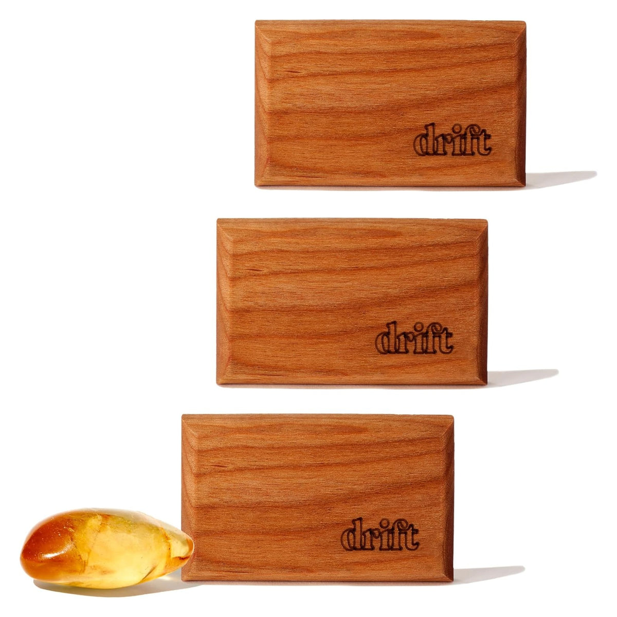 Three rectangular wood air fresheners with warm medium-brown grain, each laser-engraved with the 'drift' logo in the lower right corner. A small amber-colored resin piece sits beside the bottom unit. White background.