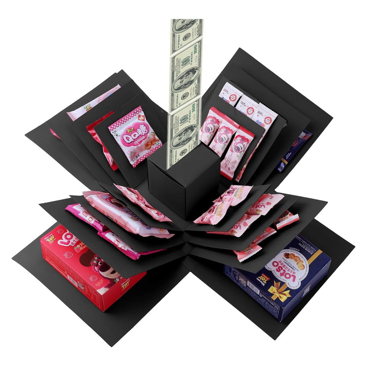 Black multi-layered explosion gift box shown open, with panels fanned out revealing assorted snacks and candies in pink and red packaging. A strip of novelty dollar bills springs upward from the center black cube.