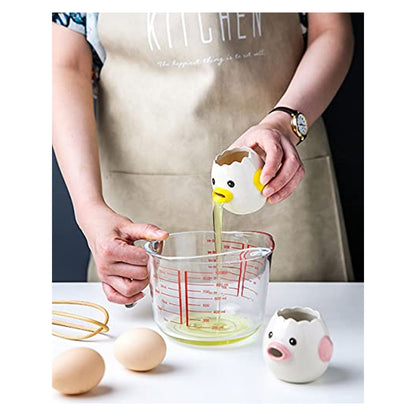 Hands using a ceramic chicken-shaped egg separator to strain egg whites into a glass measuring cup. A matching pig-shaped separator sits nearby. Two whole eggs and a whisk rest on a white surface. Person wears a tan kitchen apron.