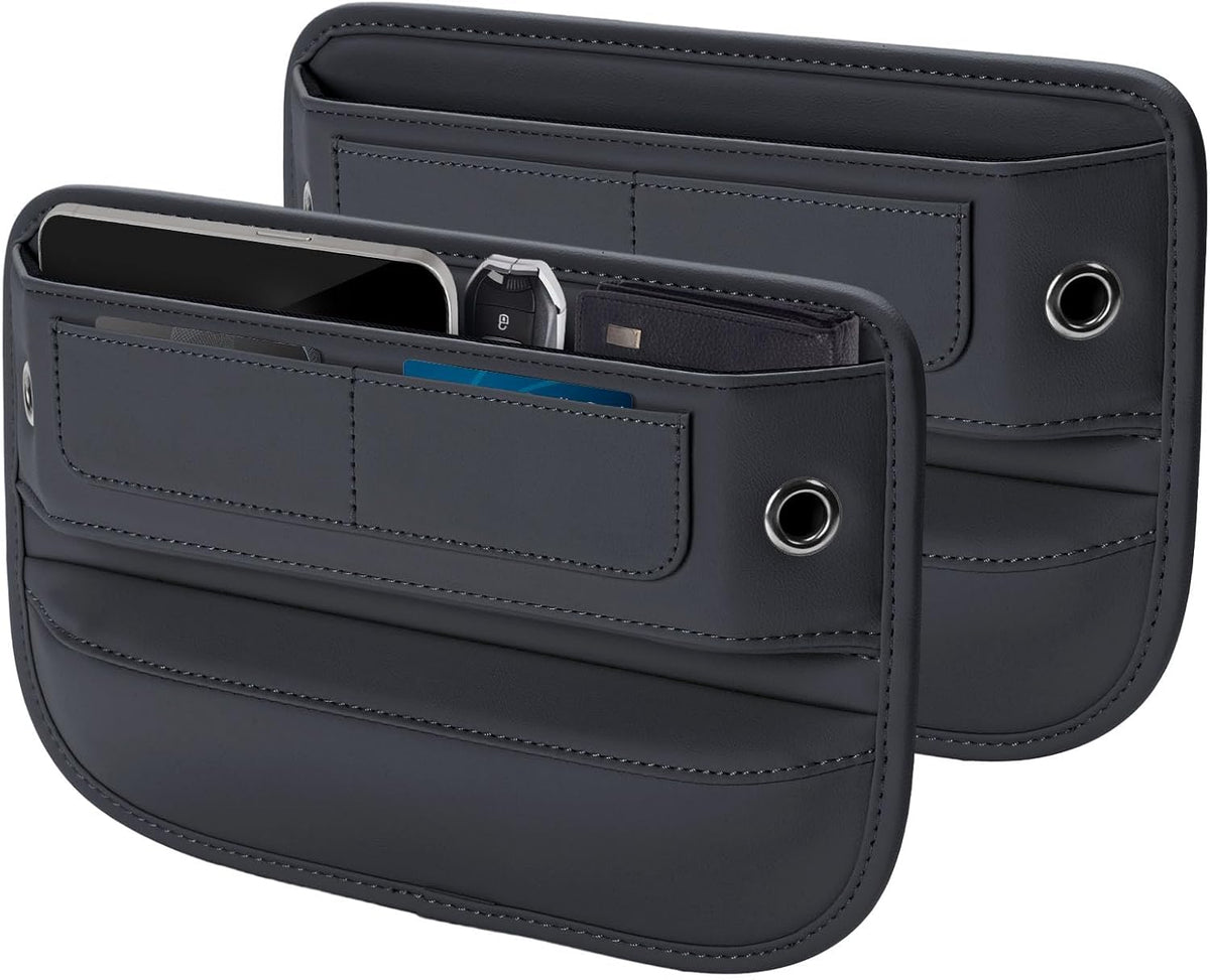 Two dark gray leather-like car seat gap filler organizers shown front and back. Each has multiple stitched pockets, a round grommet hole on the side, and a large open top slot. The front unit holds a phone, car key fob, and blue card.