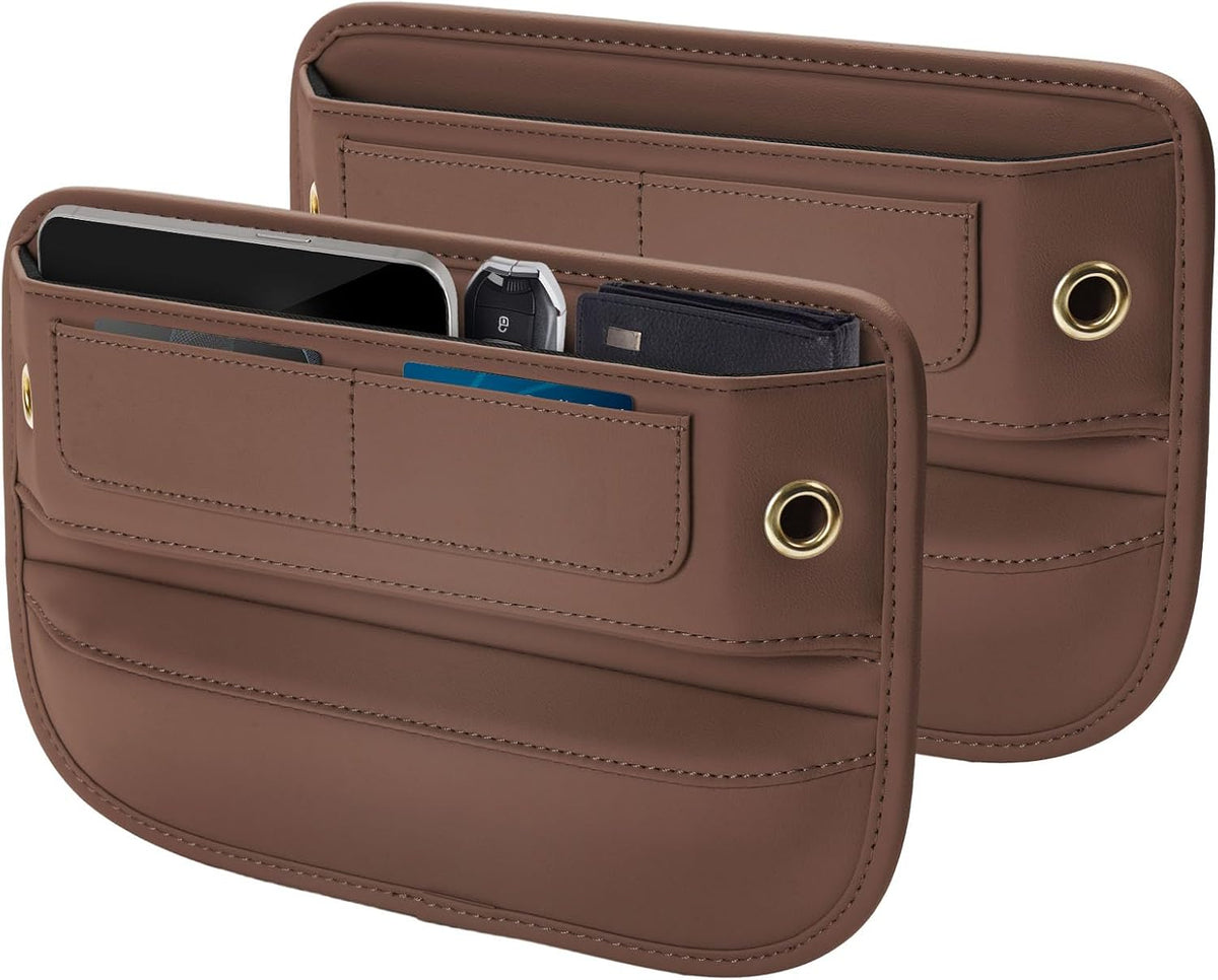 Two brown leather-like car seat gap organizers shown front and back. The front unit holds a smartphone, key fob, and cards in its open top pocket, with two horizontal card slots below and a gold-toned grommet on the right side.