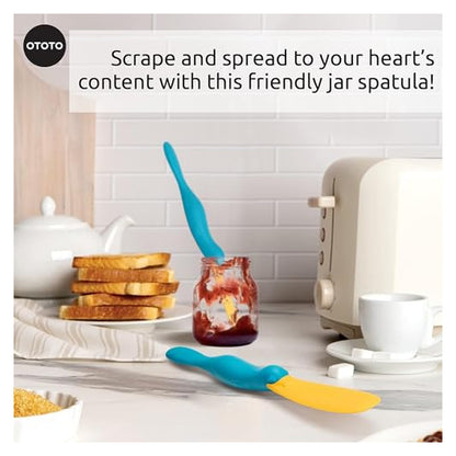 OTOTO jar spatula in teal and yellow, shaped like a platypus, shown in a kitchen scene. One spatula scrapes inside a jam jar, another lies flat on the counter. Text reads: 'Scrape and spread to your heart's content with this friendly jar spatula!'