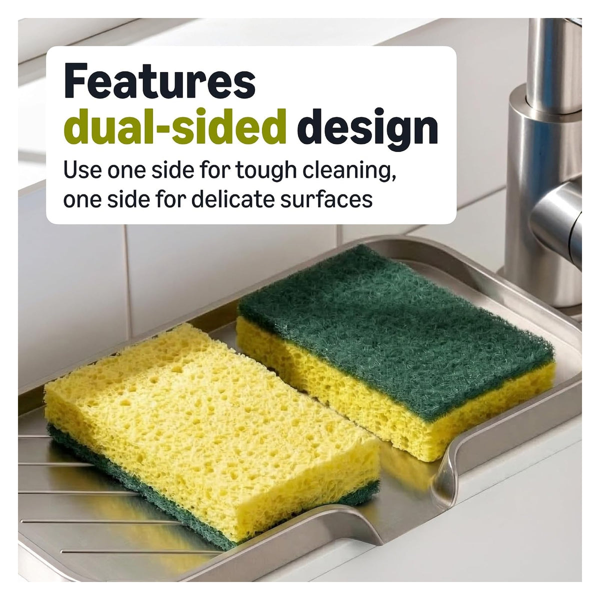 Two dual-sided scrub sponges resting on a metal sink tray, each with a yellow foam side and a dark green scrubbing pad side. Overlay text reads 'Features dual-sided design - Use one side for tough cleaning, one side for delicate surfaces.'