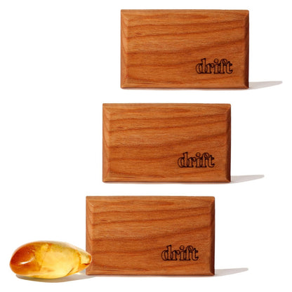 Three rectangular wood air fresheners with warm medium-brown grain, each laser-engraved with the 'drift' logo in the lower right corner. A small amber-colored resin piece sits beside the bottom unit. White background.
