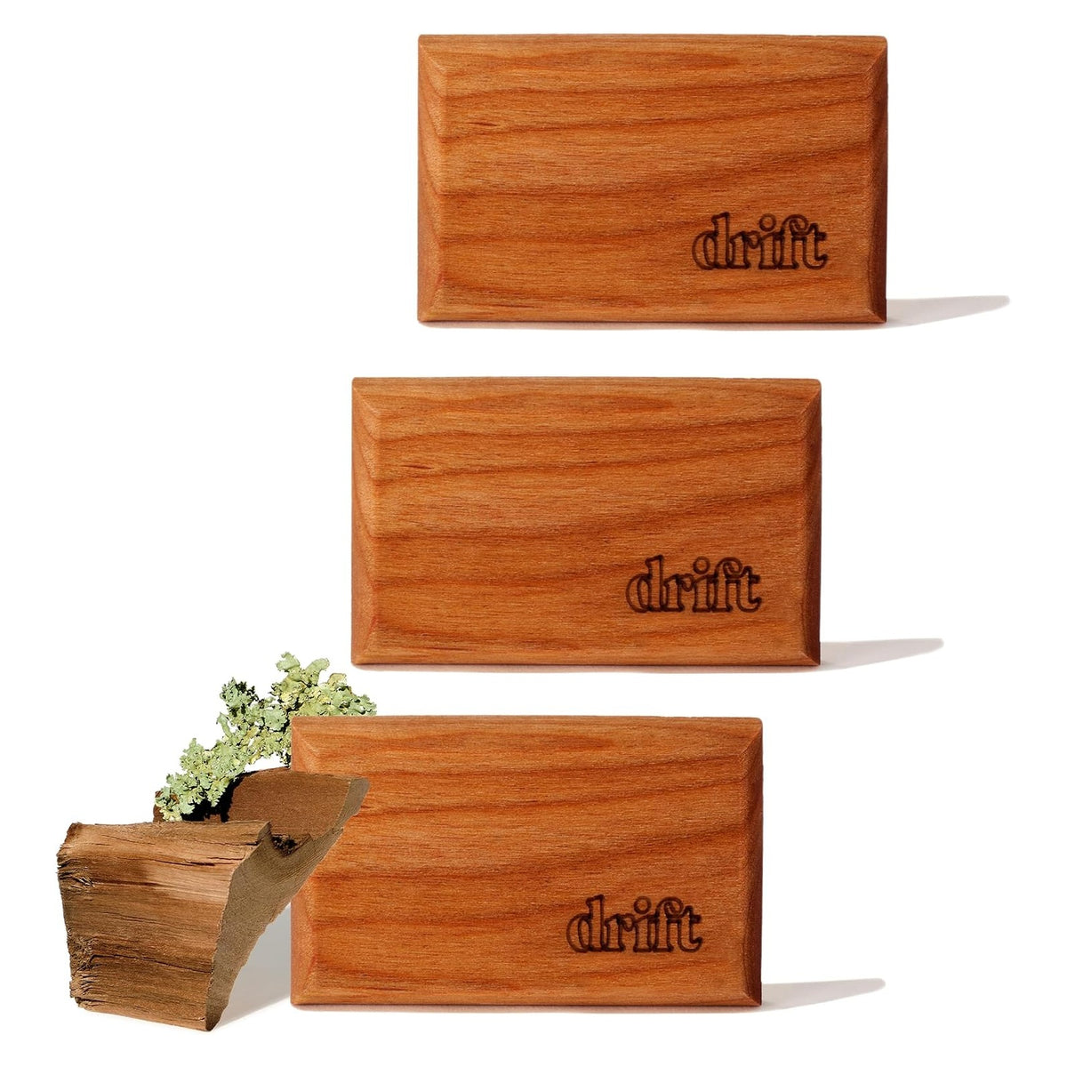Three rectangular wood air fresheners with warm medium-brown finish and visible wood grain, each laser-engraved with the 'drift' logo in the lower right corner. A piece of raw wood with lichen is shown beside the bottom unit.