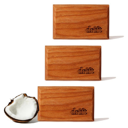 Three rectangular wood air fresheners with rounded edges, each engraved with the 'drift' logo in the lower right corner. A halved coconut sits beside the bottom unit, suggesting the Cabana scent. Shown on white background.