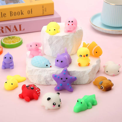 Collection of small colorful kawaii animal squeeze toys arranged on white stone risers and a pink surface, including a purple starfish, yellow duck, panda, green crocodile, red crab, purple cat, and more cute characters with smiley faces.
