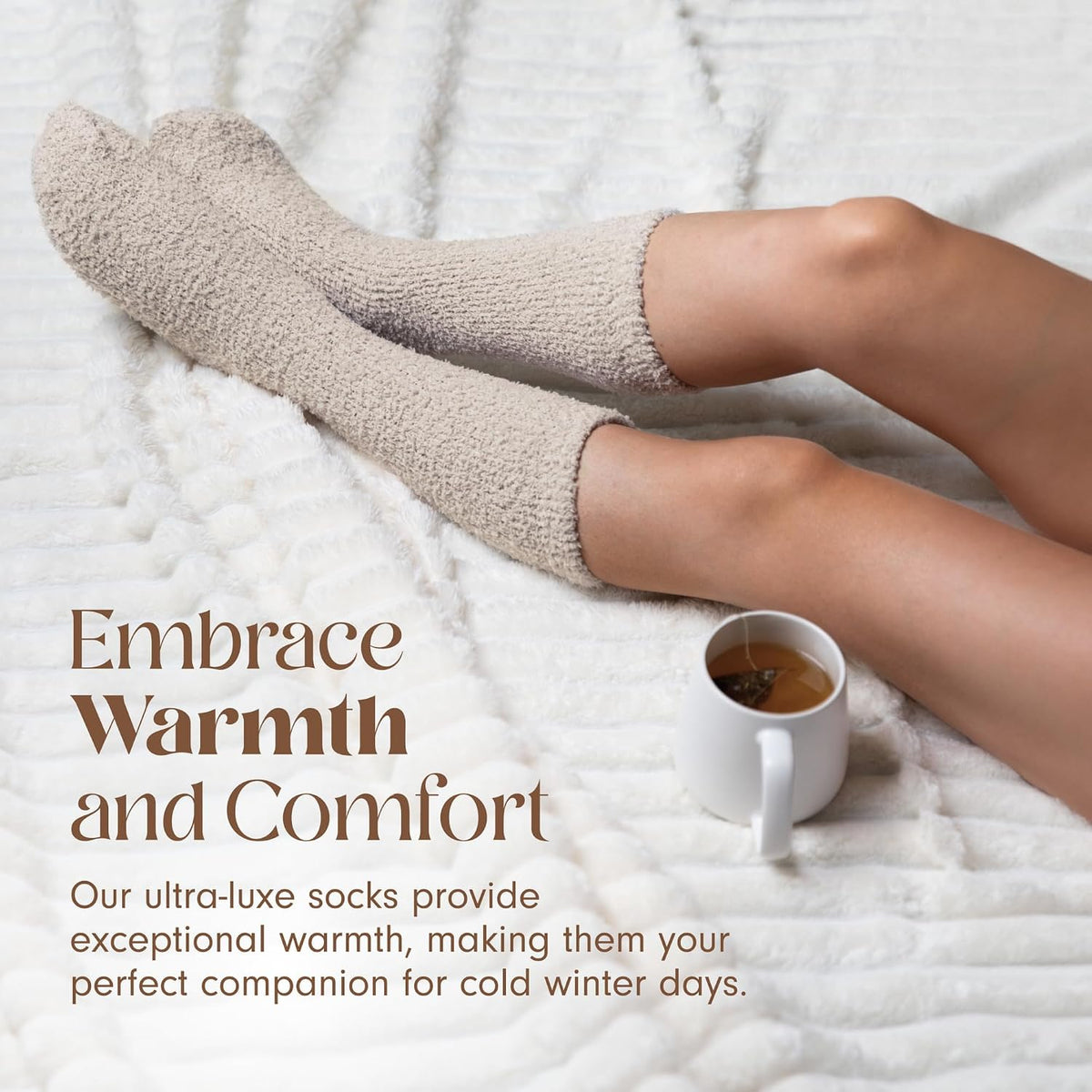 Legs resting on a white textured blanket wearing fluffy cream-colored knit socks, beside a white mug of tea. Text reads 'Embrace Warmth and Comfort' with a tagline about ultra-luxe socks for cold winter days.