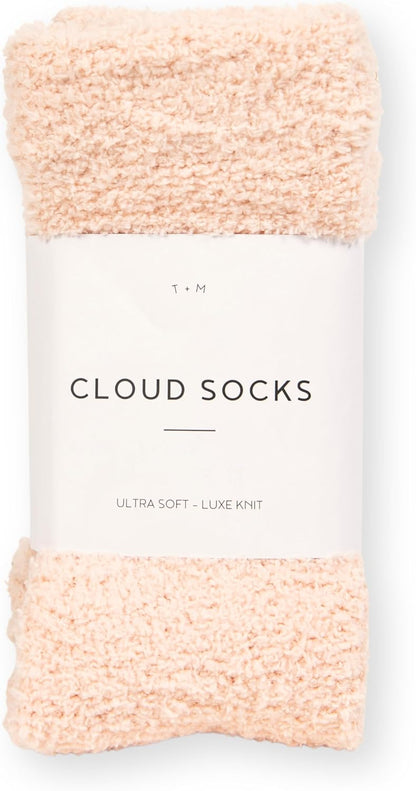 A folded pair of pale pink fuzzy socks with a fluffy, bouclé-style knit texture, wrapped with a white paper band label reading 'Cloud Socks' and 'Ultra Soft - Luxe Knit' by T+M.