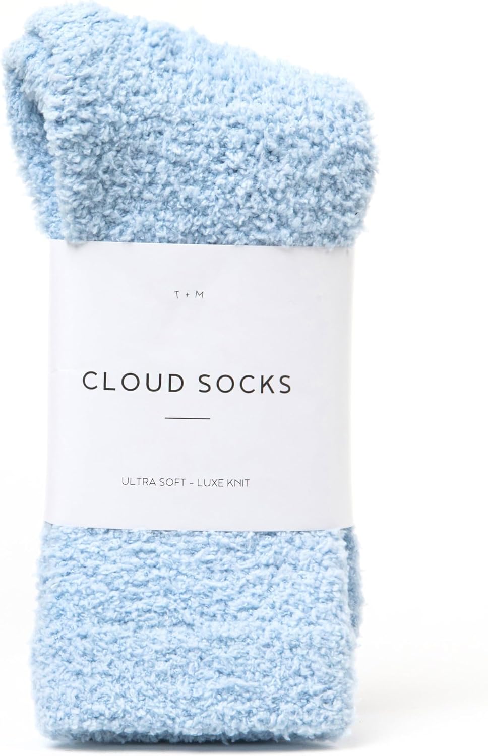 A pair of fluffy light blue socks folded and wrapped with a white paper band label reading 'Cloud Socks' and 'Ultra Soft - Luxe Knit' by T+M, shown against a white background.