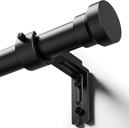 Matte black curtain rod shown at an angle with a cylindrical flat-top finial on the right end, resting in a wall-mounted L-bracket with two visible screws. A set screw is visible on the rod near the bracket.