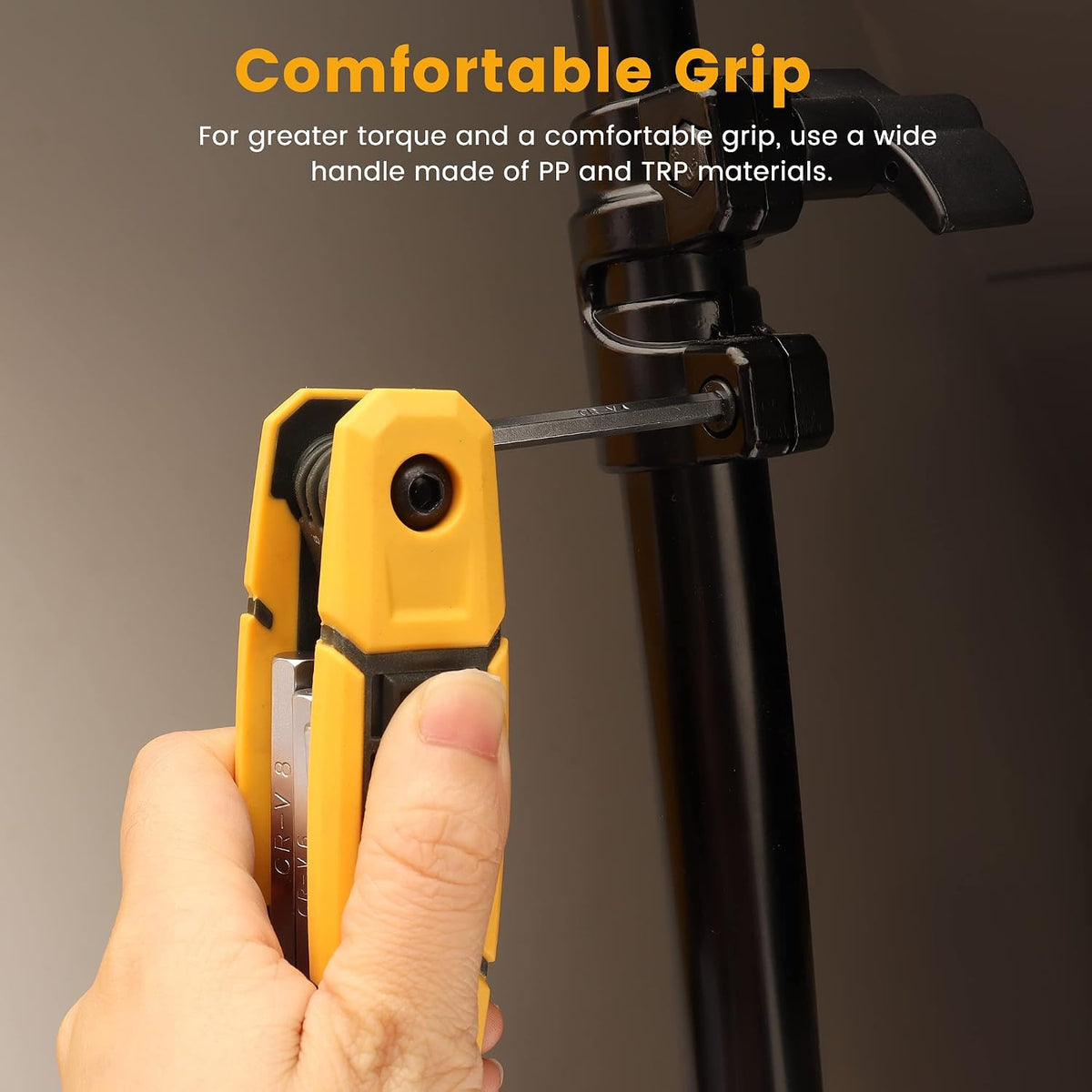 Hand holding a yellow and black folding hex key tool, inserting a small allen wrench into a black metal clamp on a pole. Text reads 'Comfortable Grip' with a note about PP and TRP handle materials.