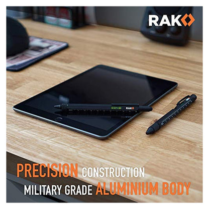 Two black RAK multitool pens on a wood desk, one resting on a tablet showing a ruler scale, spirit level, and RAK logo. Text reads 'Precision Construction Military Grade Aluminium Body'.